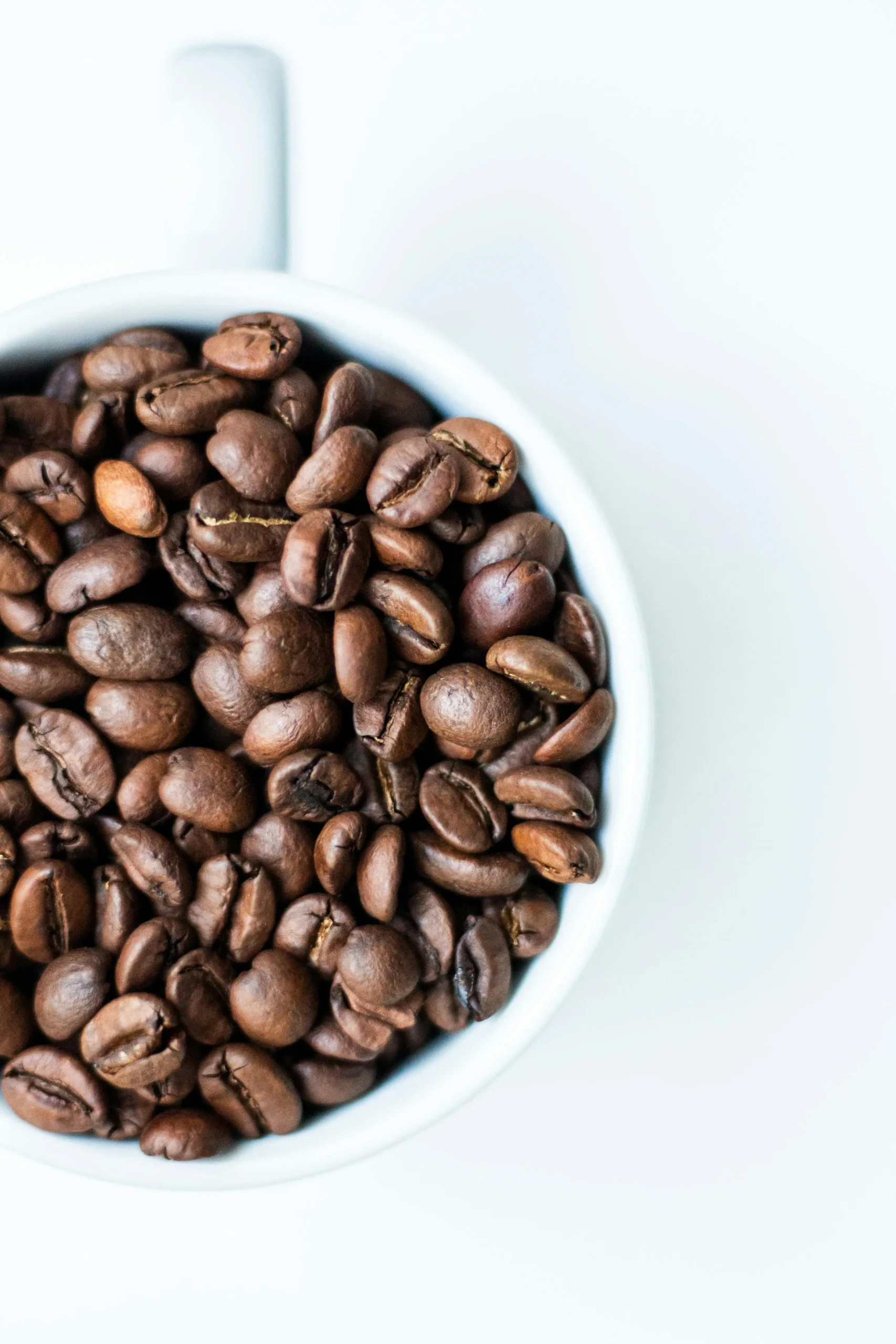 Frisch geröstete Espresso Bohnen in einer Holzschale neben einem Siebträger-Espresso mit cremiger Crema – Röstvergleich Arabica vs. Robusta